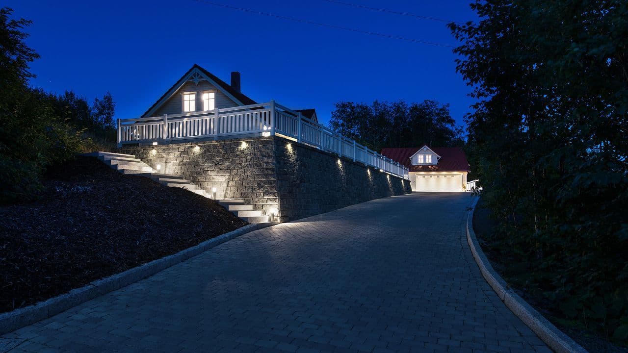 Stemningsbilde kveld. Hus med stor steinbelagt uteplass og lys i mur.