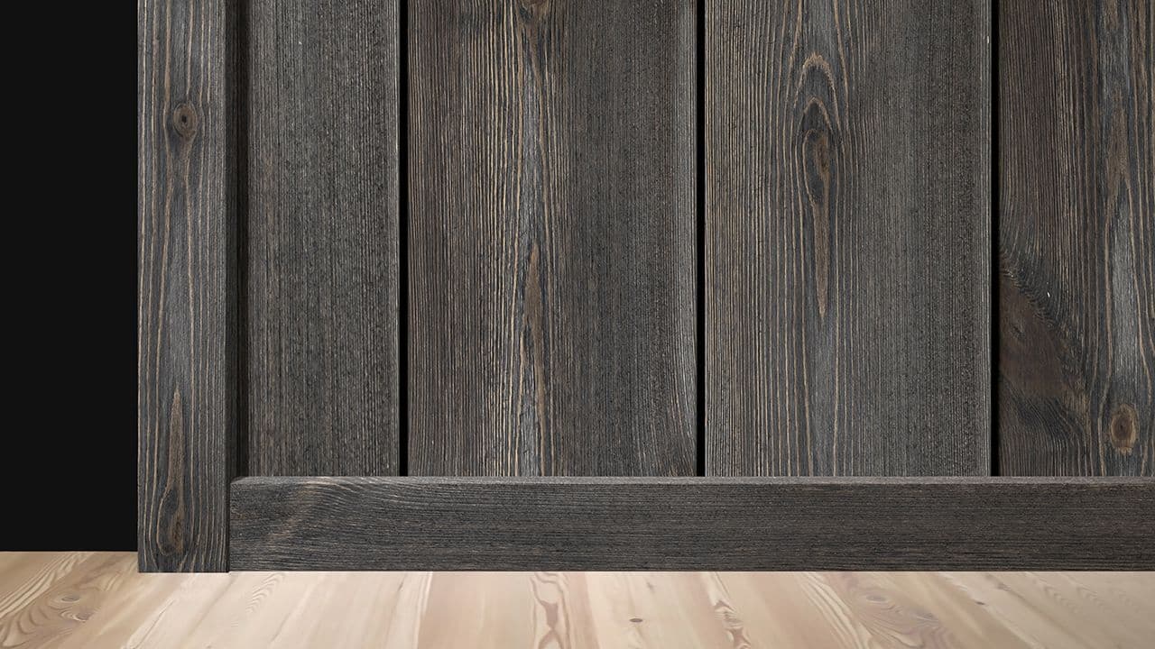 Nærbilde av vegg med trepanel og listverk i samme beisfarge.