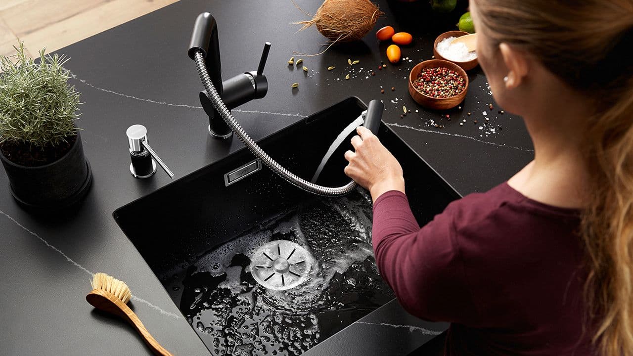 Kvinne som holder smart blandebatteri i sort med uttrekk og skyller vasken.