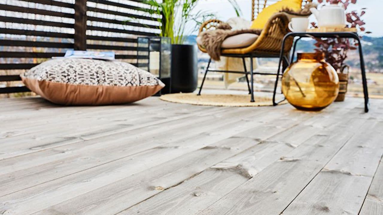 Koselig uteplass med kurvstol, teppe og grønn plante i hjørnet av en terrasse