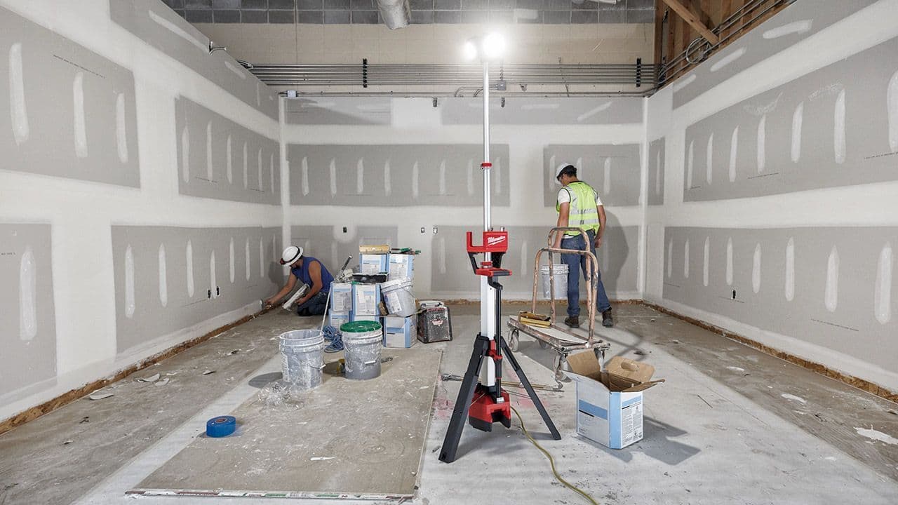 Håndverkere arbeider med gipsvegg i et rom under oppussing, med et rødt Milwaukee lasernivellerings-verktøy på stativ i forgrunnen