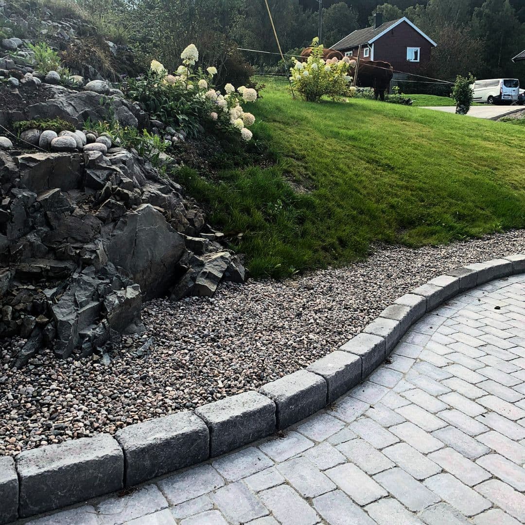 Steinbelagt innkjørsel med pyntestein langs kant mot gressplen