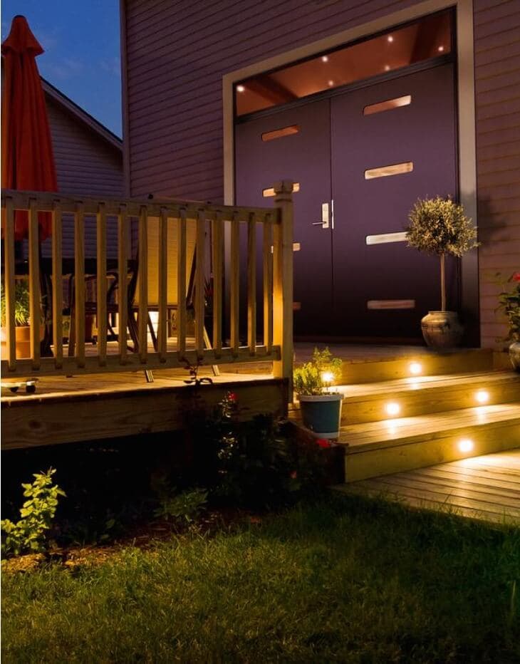 Tofløya ytterdør i grå farge og inngangsparti med opplyst trapp.