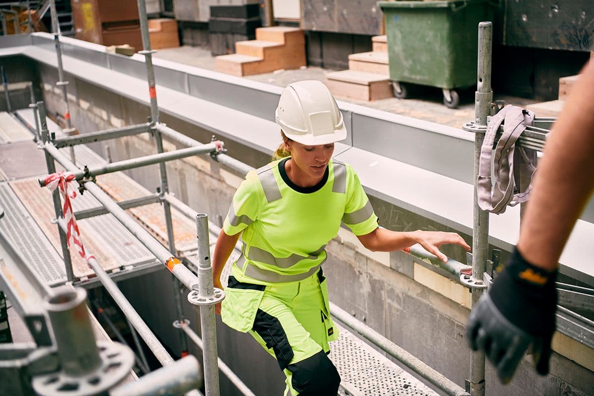 kvinnelig håndverker i high-vis arbeidsklær går opp et stillas