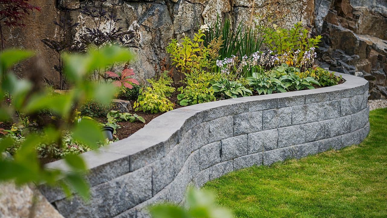 Hageideer skråning: blomsterbed bygget av mur med bølgete form i norsk hage.