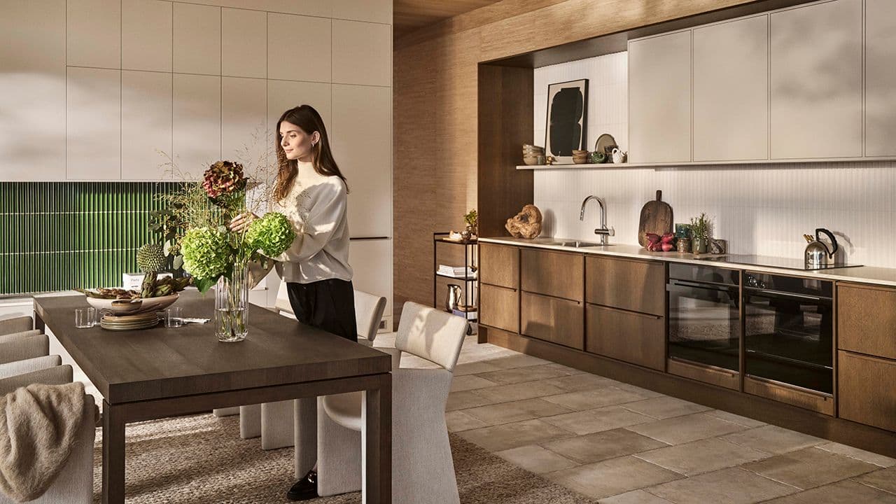 Dame som steller med blomster i et kjøkken med eike- og lyse fronter.