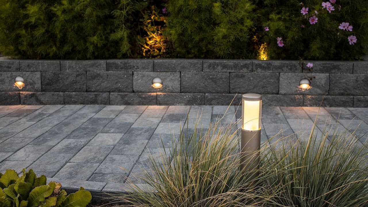 Norsk hage med utebelysning i mur langs gangsti.