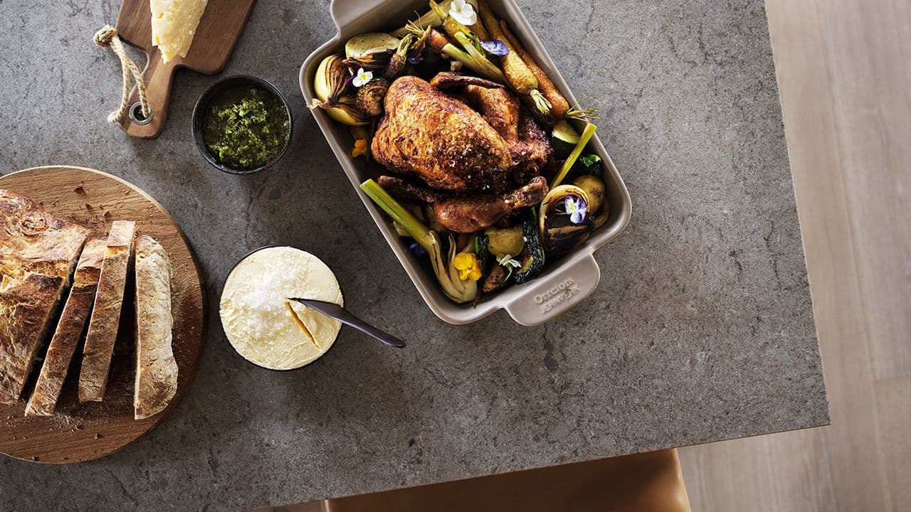 Benkeplate i stein sett ovenfra på kjøkkenøy med kyllingmiddag servert i ildfast form.