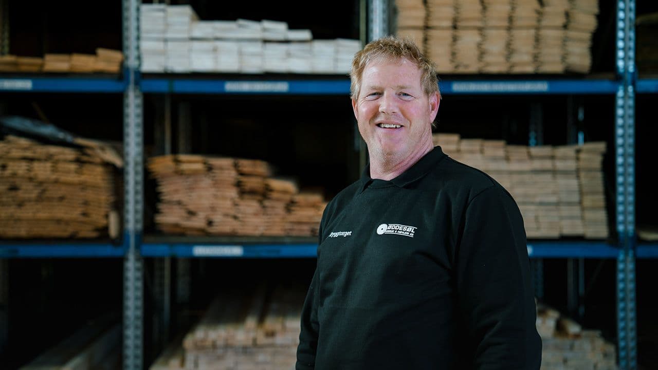 Byggtorget-ansatt i byggevarehus foran hylle med trevirke.