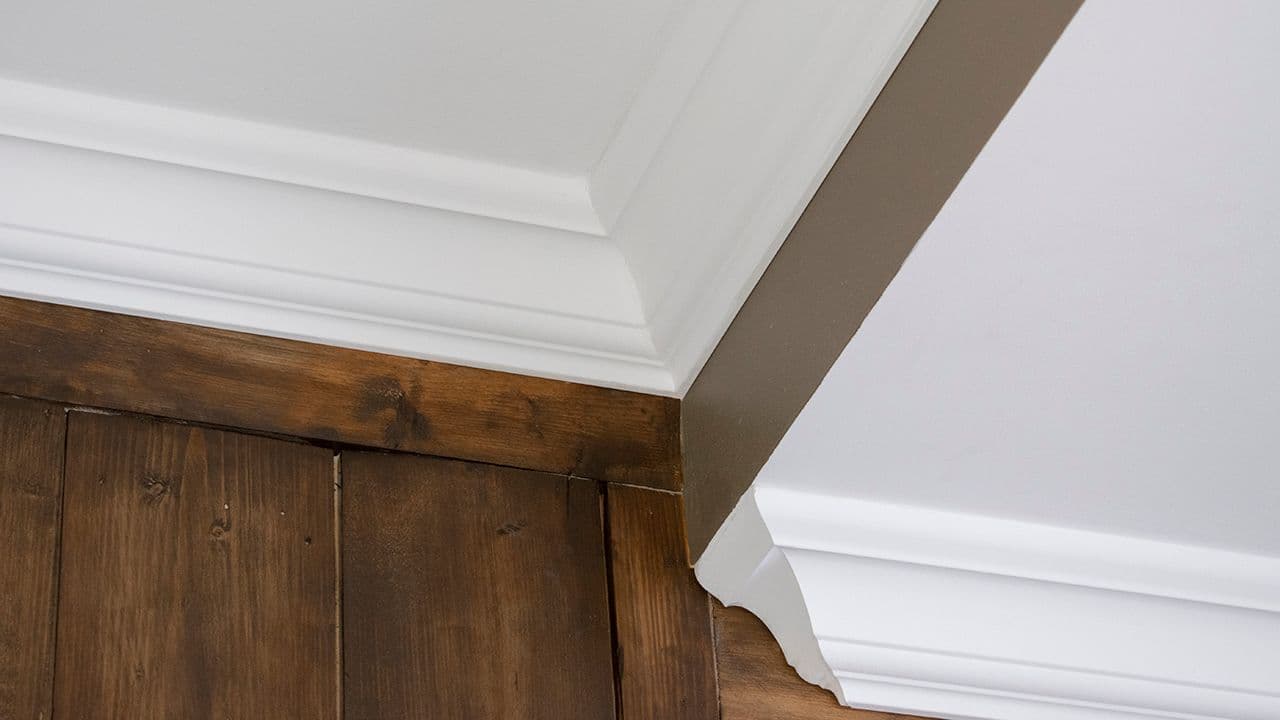 Hvite profilerte taklister mot trevegg.