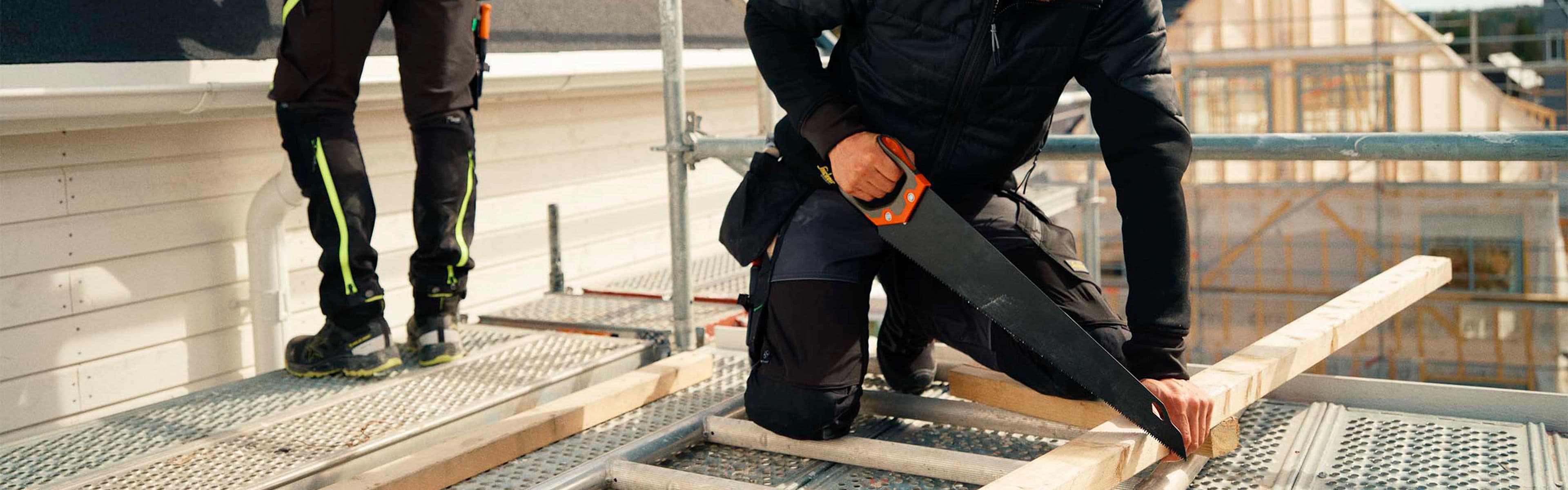 Håndverkere som arbeider med tak og sager på stillas med arbeidsklær.