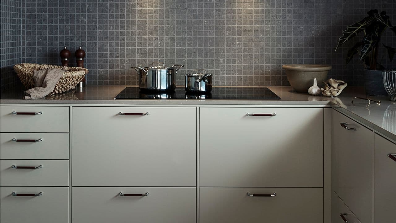 Lysegrønt hyttekjøkken i klassisk stil med stålkasseroller på koketoppen.