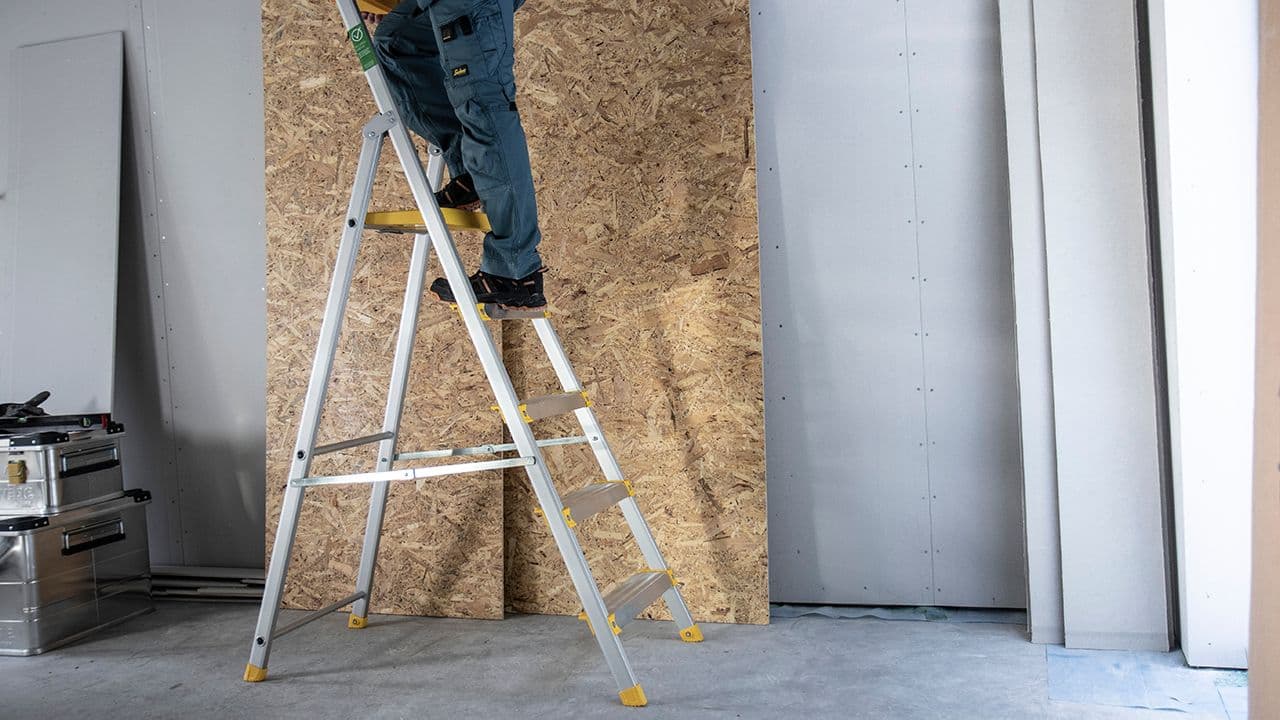 Mann som står på gardintrapp for å komme bedre tl i høyden på byggeplass.